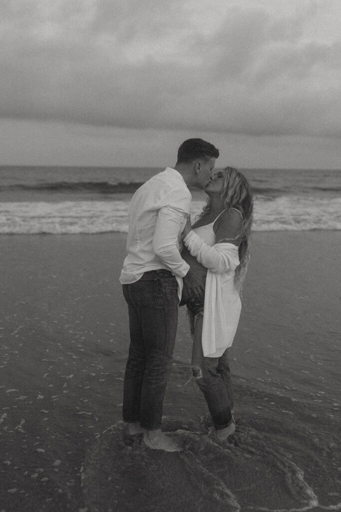 husband and wife on beach kissing for maternity photos