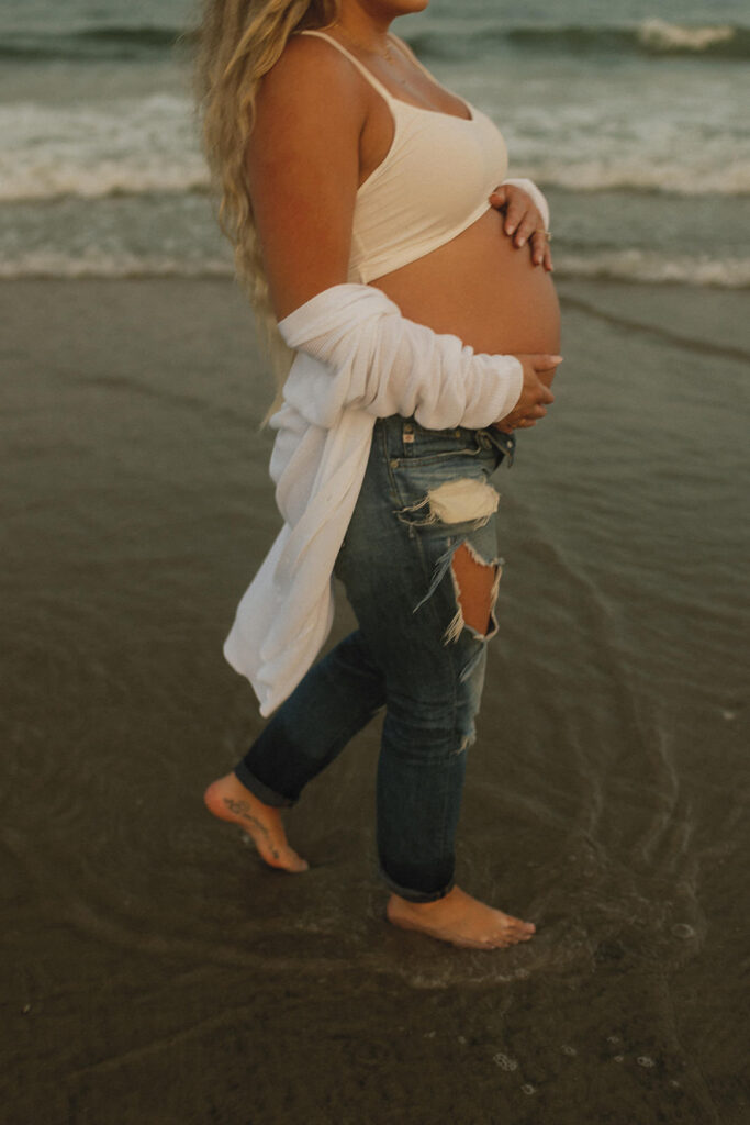 pregnant mom walking on the beach holding her belly for her New Jersey Maternity Photoshoot