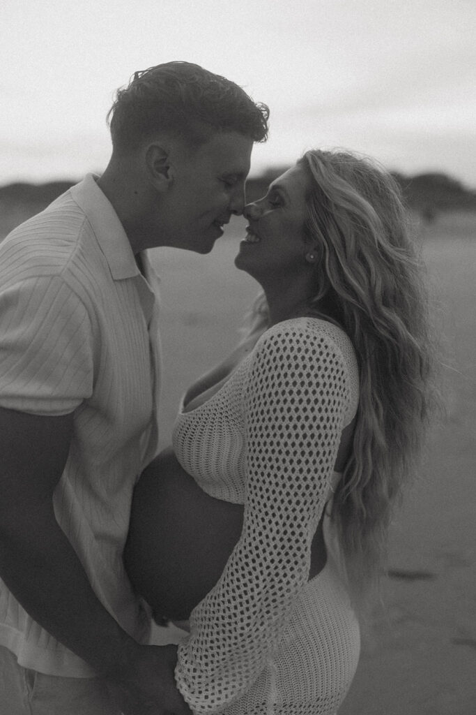 husband and wife standing belly to belly with their noses touching smiling for maternity photos in NJ