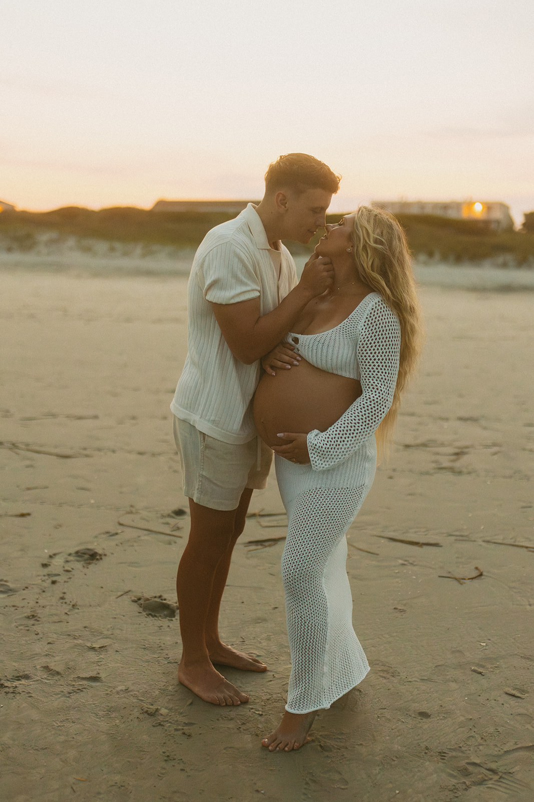 Couple on the beach in New Jersey facing each other and kissing for their maternity photos