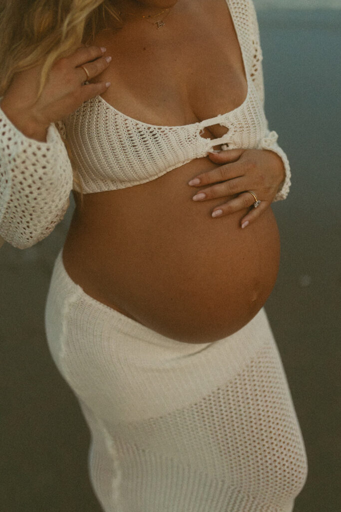 up close photo of pregnant belly with her hand on the top of her belly in a white knit two piece set