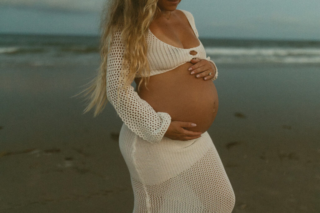 Pregnant mama in a white knit two piece set holding her baby belly for a photo