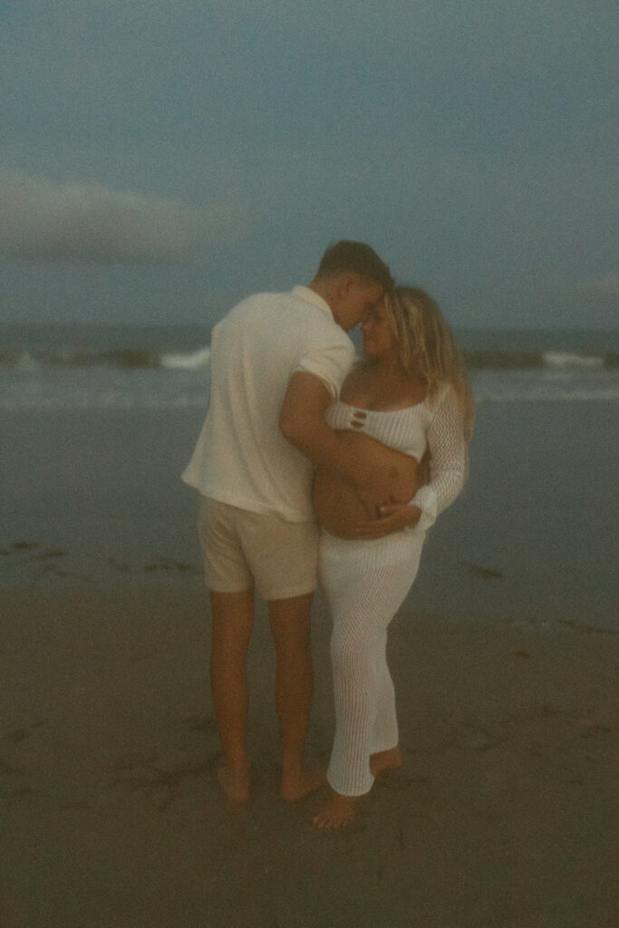 husband and wife on beach posing for maternity photos