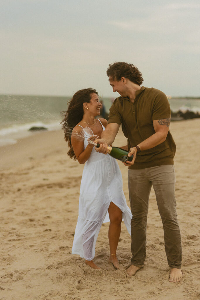 Couple popping a bottle of champagne on the beach 